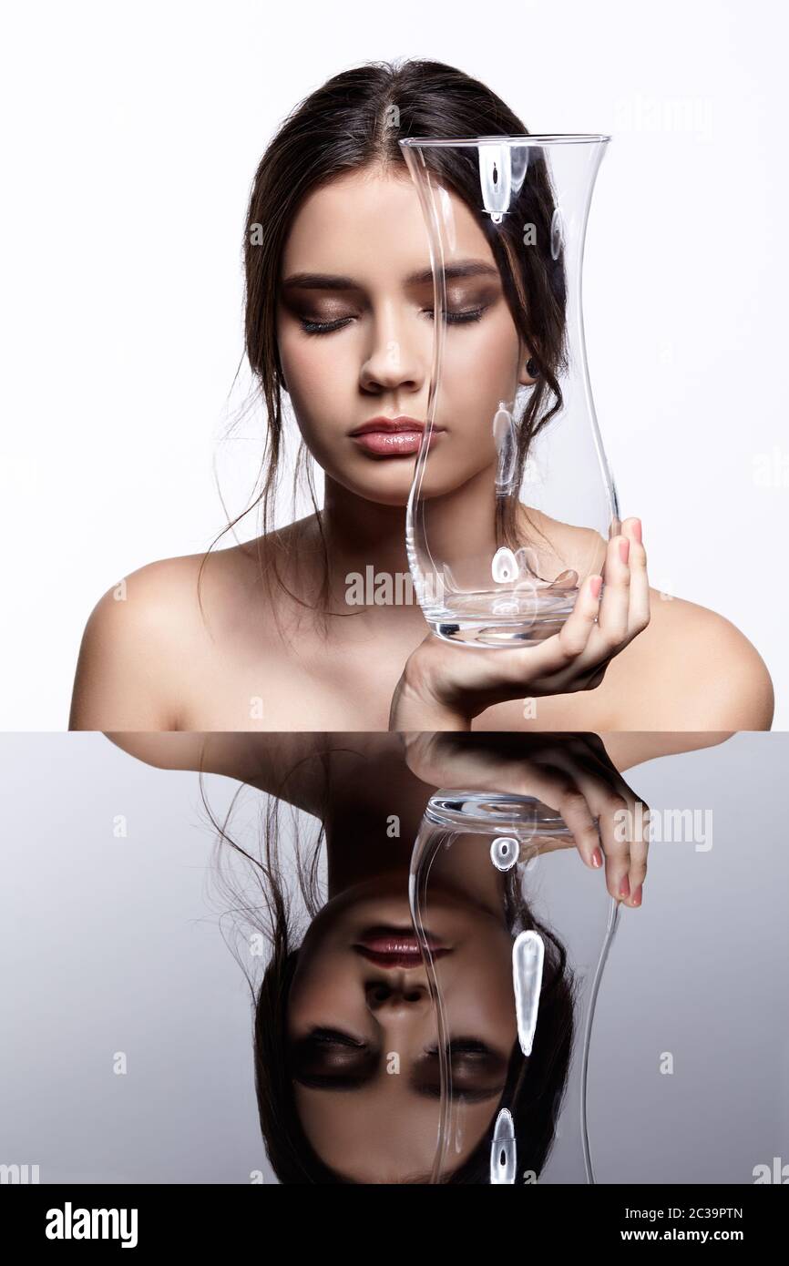 Girl hides her face behind a glass vase. Beauty portrait of young woman