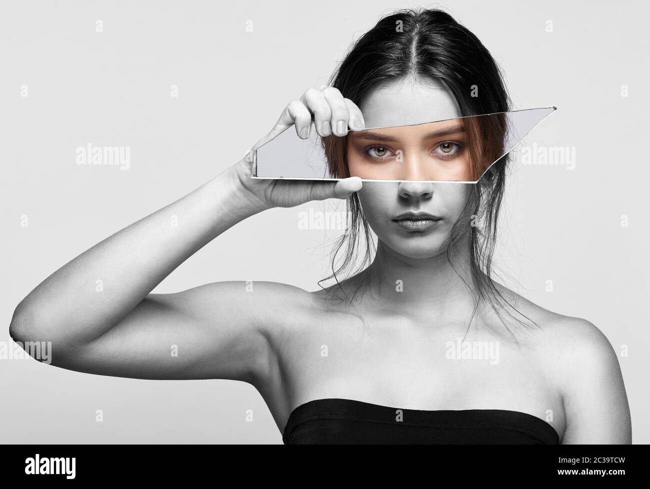 girl covers her face with a shard of the mirror female with mirror shard in hand posing on gray background 2C39TCW