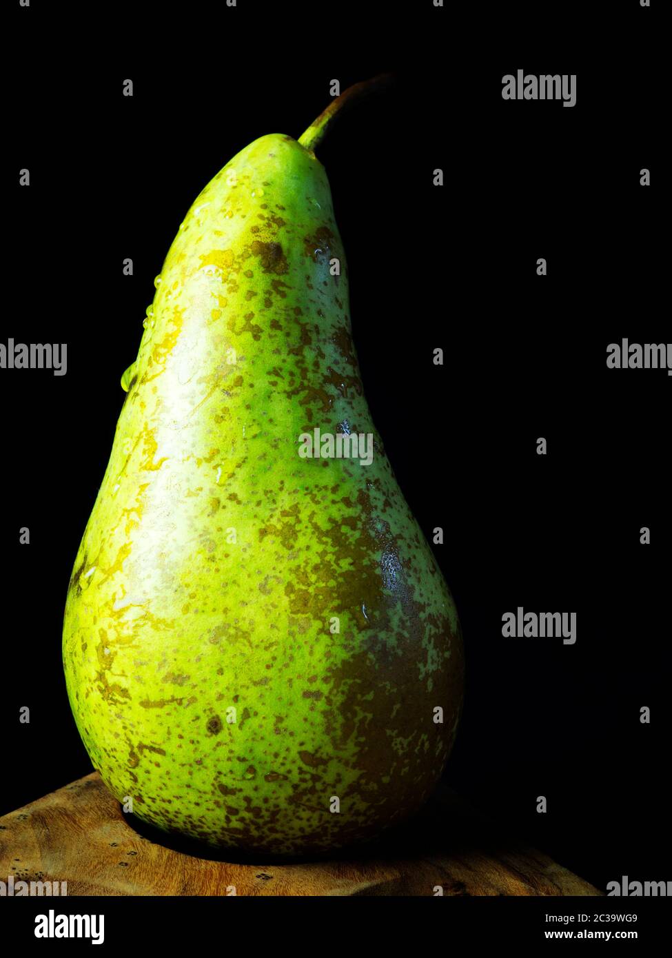 A single washed conference pear with water droplets on a wooden dish against a black background Stock Photo