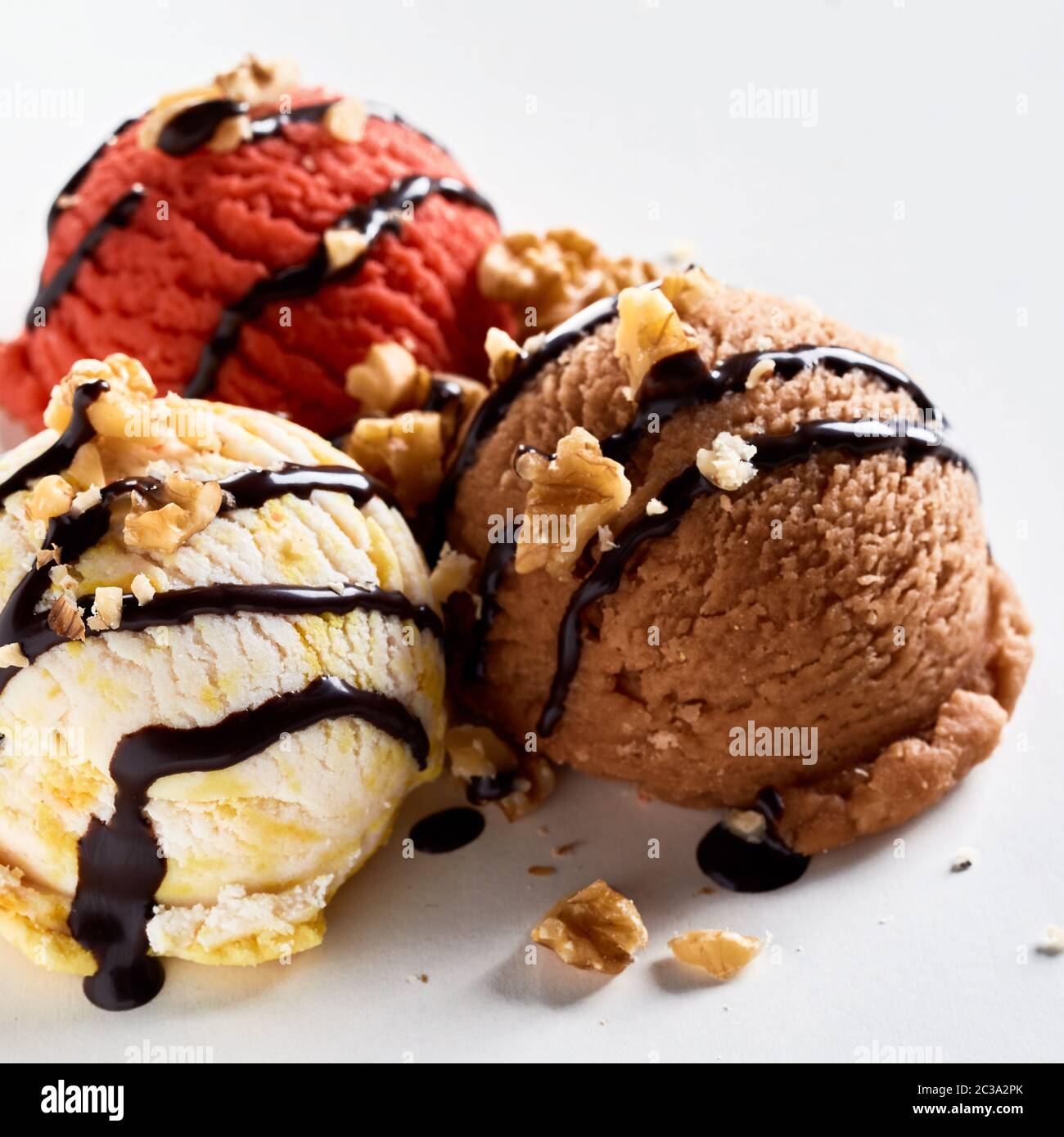 Three scoops of flavored frozen ice cream topped with chopped walnuts and drizzled chocolate in a close up view Stock Photo