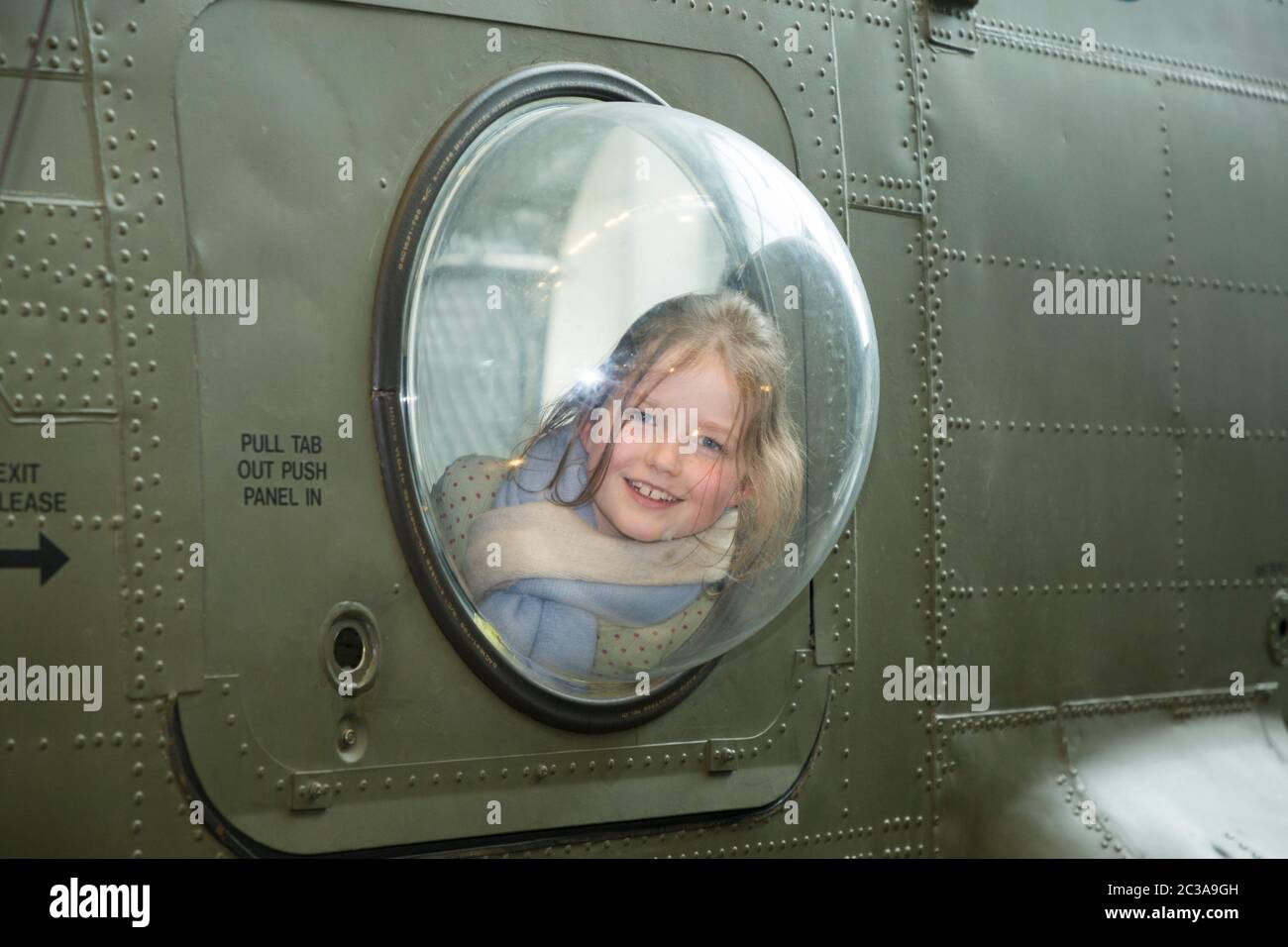 Visitor tourist / children / child / girl looks out of plexi glass bubble window of a Boeing Chinook HC2 helicopter, aircraft. RAF Royal air force museum, Hendon London UK (117) Stock Photo