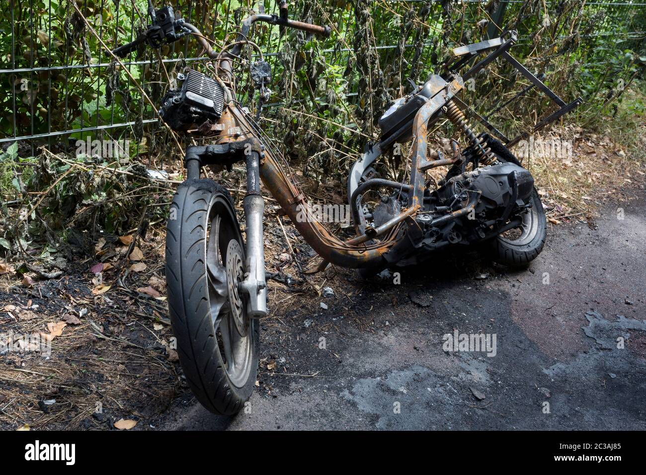 The wreckage of a burned-out scooter leans abandoned against fencing in ...