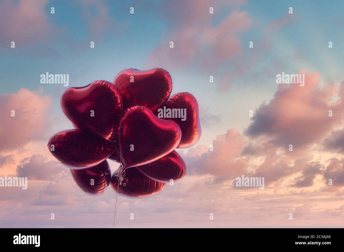 Group of heart shaped red air baloon on dramatic sky with pink clouds. Valentine's day and romance concept. Stock Photo