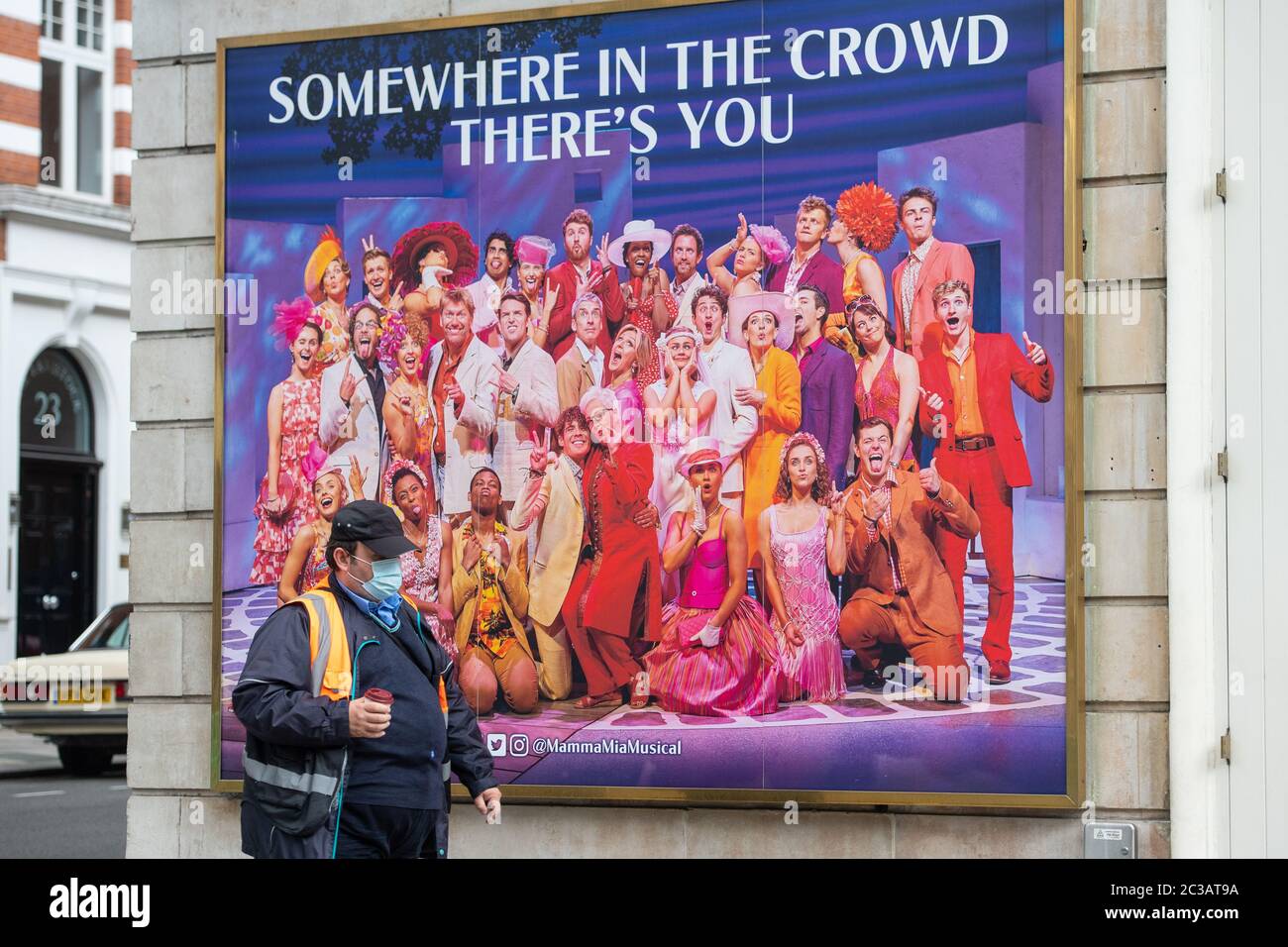 A man wearing a protective face mask passes a poster for 'Mamma Mia' outside the Novello theatre in central London, as theatres remained closed for performances due to coronavirus lockdown measures. Many productions have taken the decision to not reopen until 2021 and it is expected to take several months of preparation for the productions to be remounted and audience confidence and advance sales to build once social distancing restrictions are lifted for theatres. Stock Photo