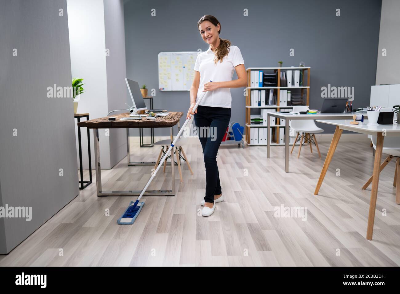 Full Length Of Female Janitor Mopping Floor In Office Stock Photo