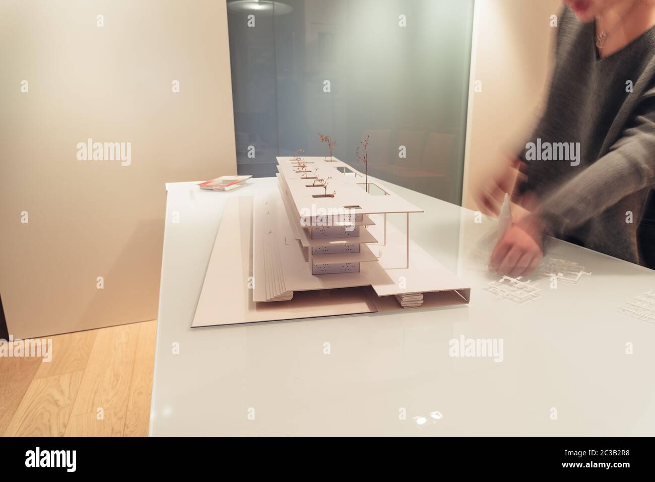 Female architect working on architecture model made with cardboard on table in office of architectural firm. She is moving, motion blurred. Stock Photo