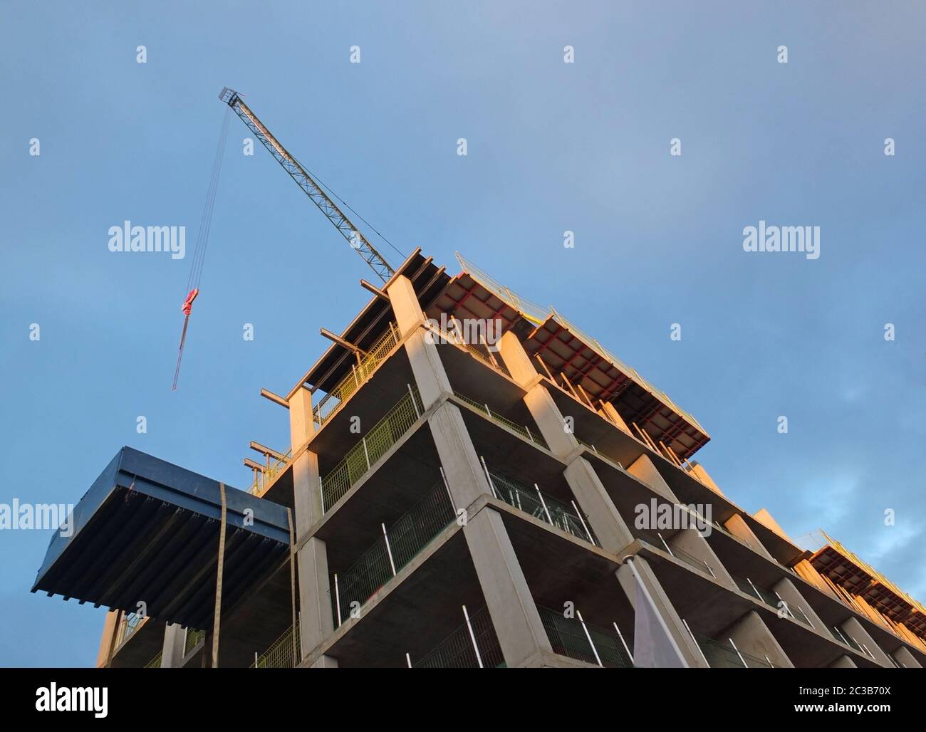 a vertical corner view of a crane on a construction site with a concrete framework against a blue sunlit sky Stock Photo