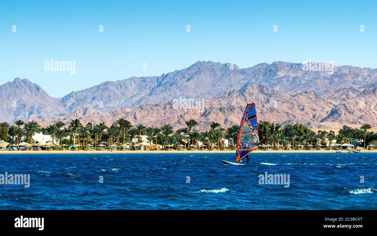 windsurfer rides in the sea on the background of the beach with palm trees and high rocky mountains Stock Photo
