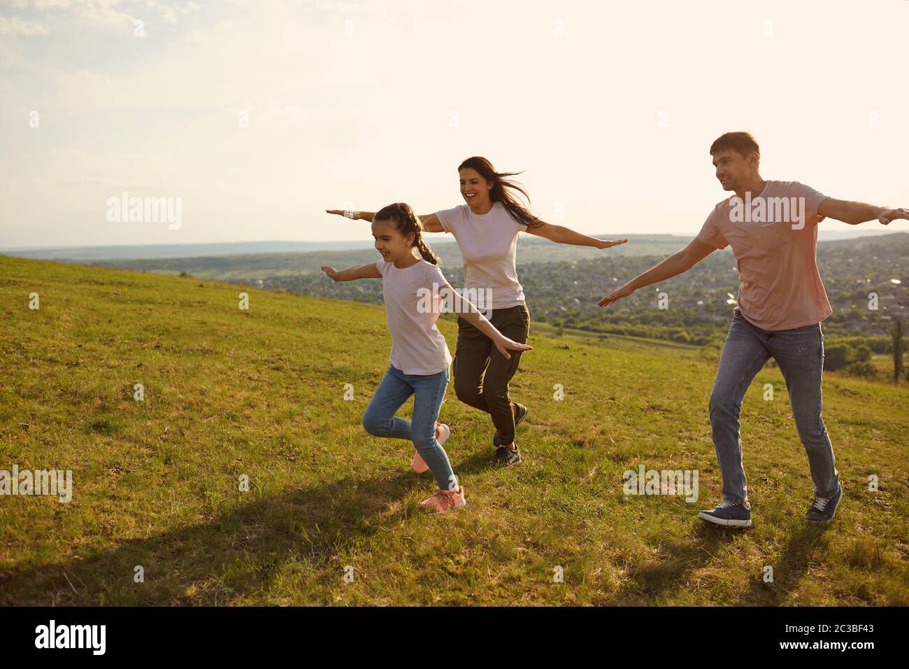 A positive family cheerfully runs across the field hands to the side in the morning at dawn in the sun. Stock Photo