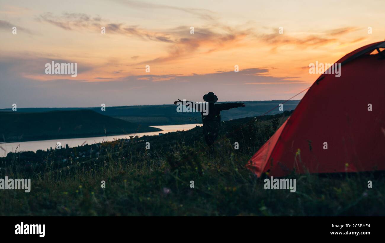 Girl near the tent at sunset with hands up. Stock Photo