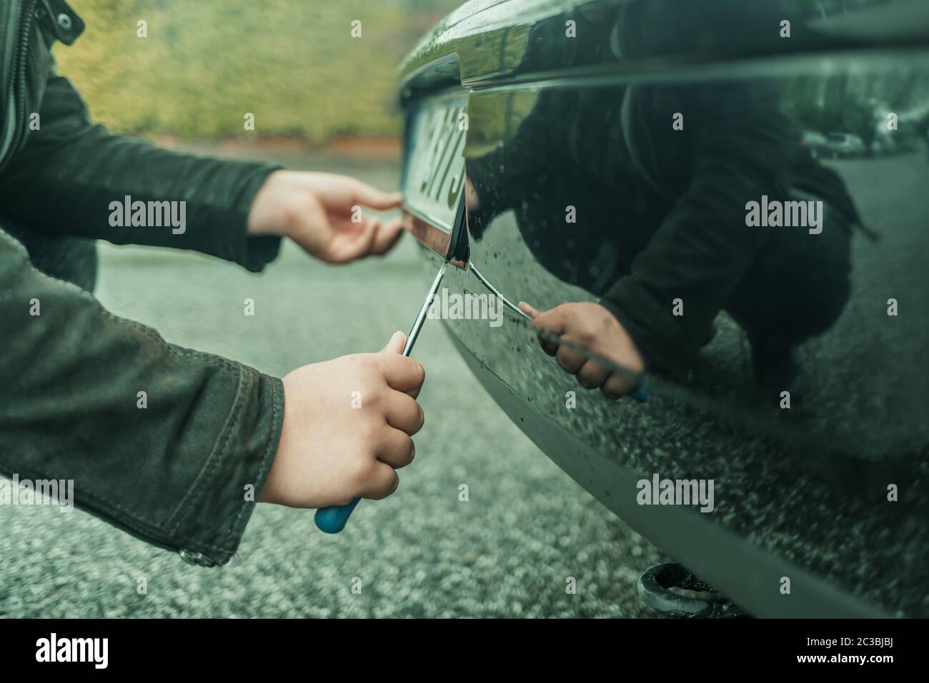 A person steals the license plate on a parked car with a screwdriver