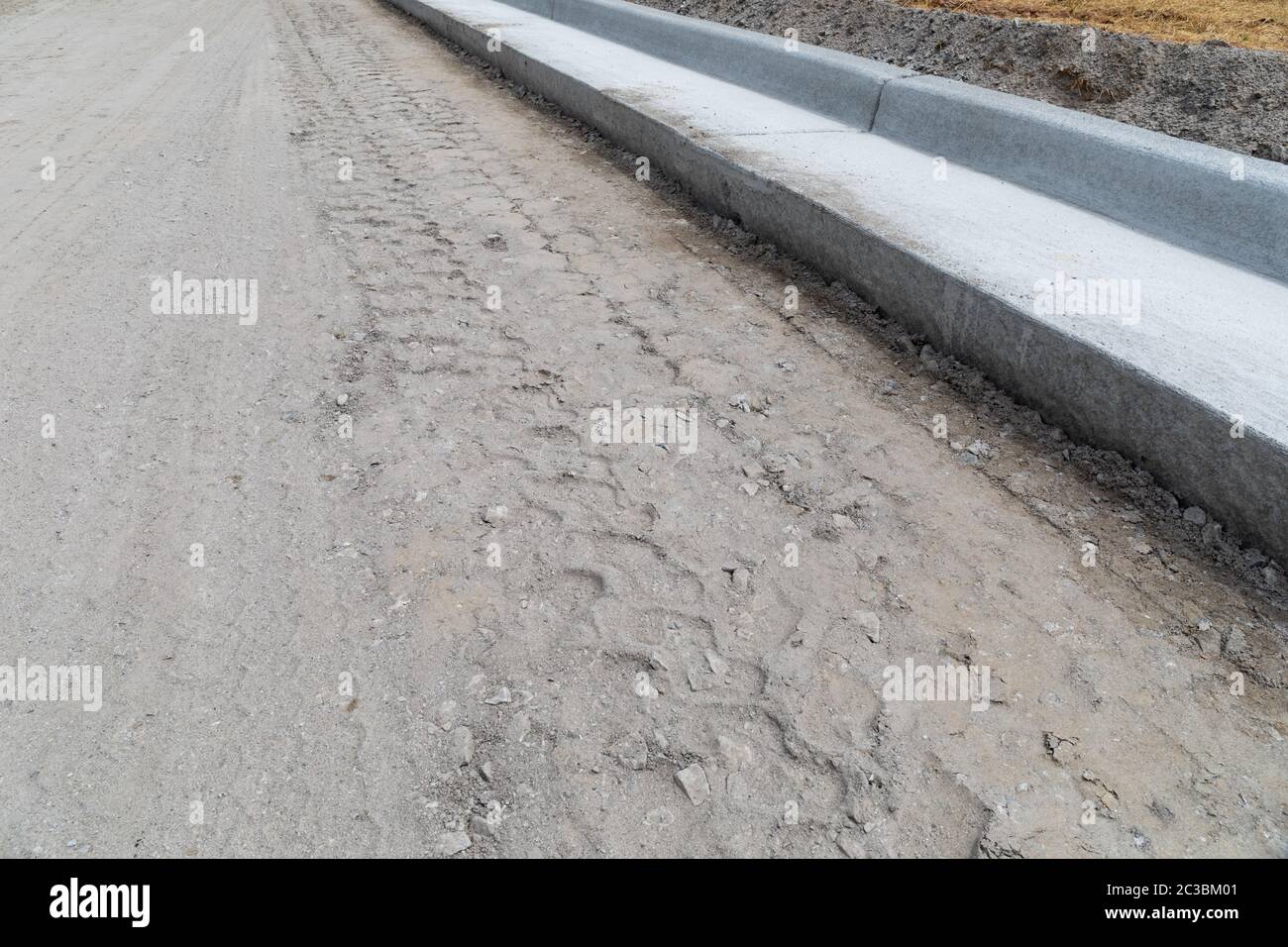 Freshly graded road bed next to new extruded concrete curb, street construction site, horizontal aspect Stock Photo