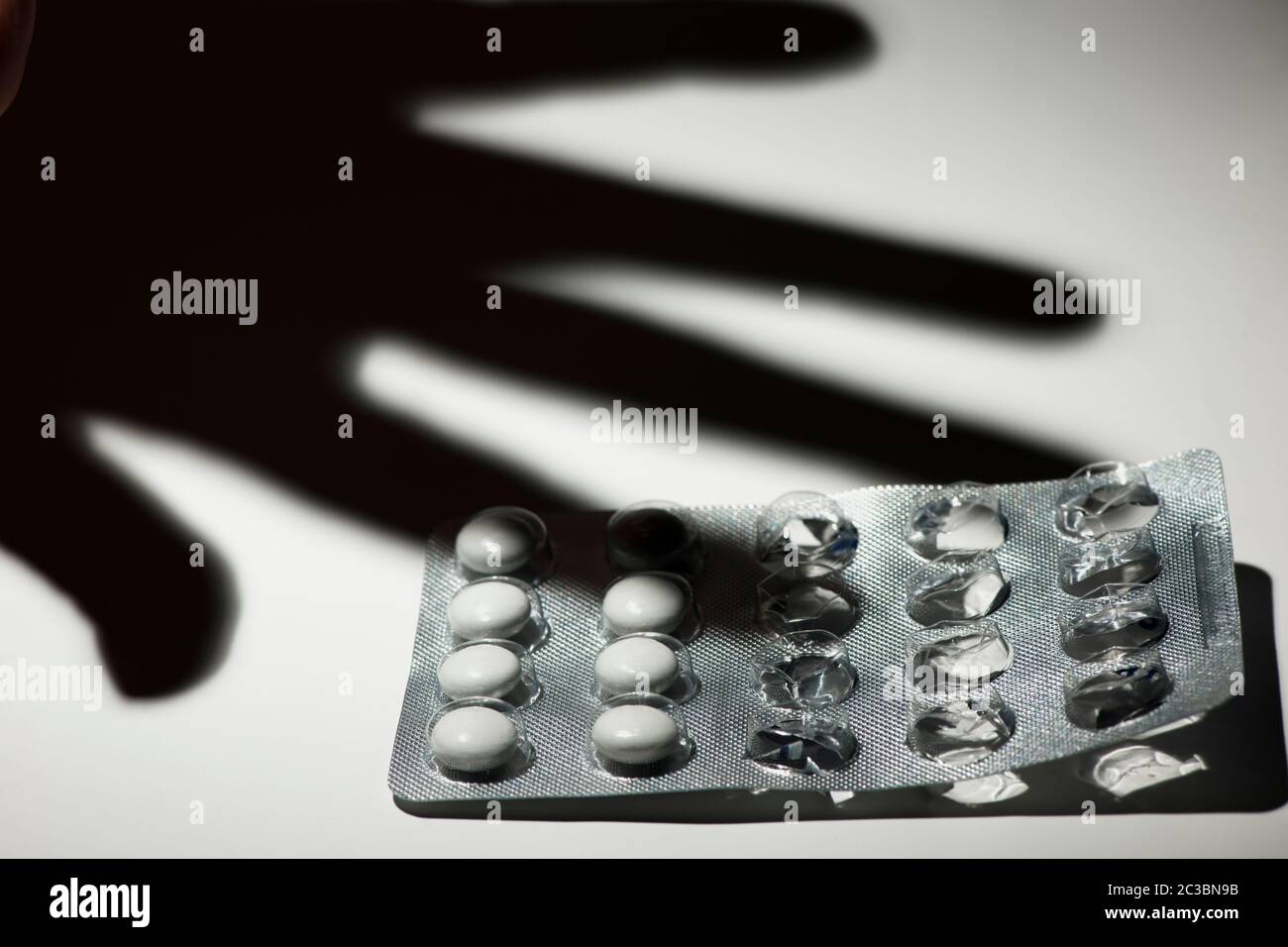 Started pack of tablets with shadow of a hand on white background in monochrome appearance. Stock Photo