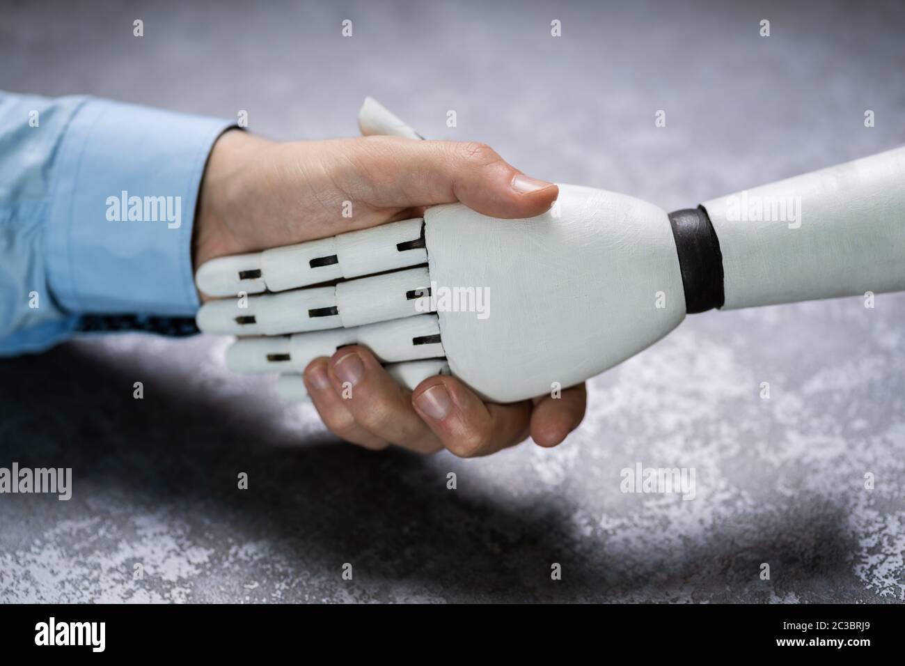 Close-up Of Digital Generated Human Hand And Business Man Shaking Hands Against Grey Background Stock Photo