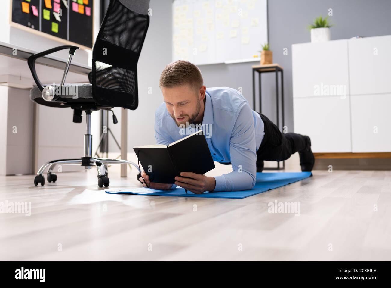 Businessman Reading Notes While Doing Plank Exercise In Office Stock Photo