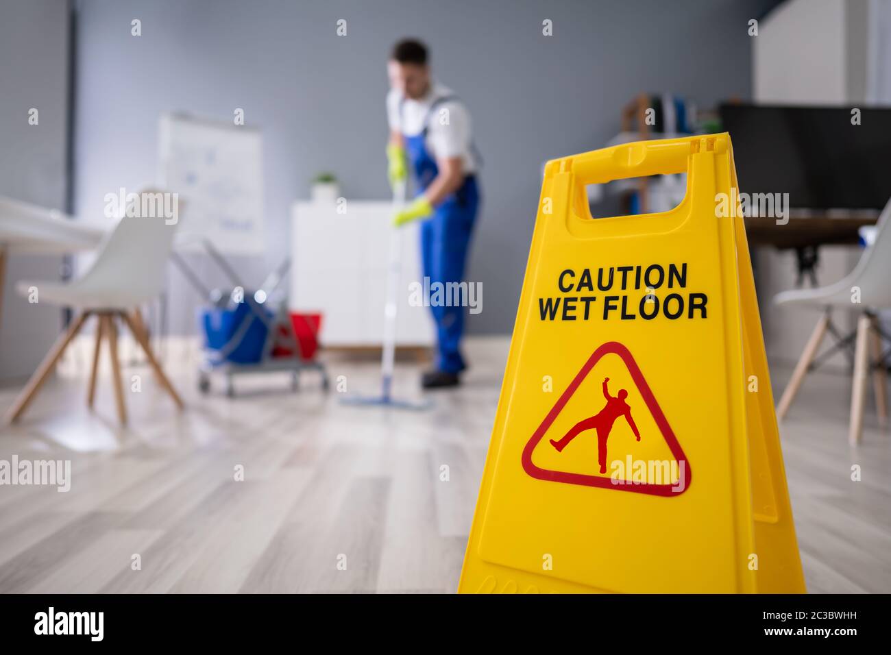 Close-up Of Man Cleaning The Floor With Yellow Wet Floor Sign Stock Photo