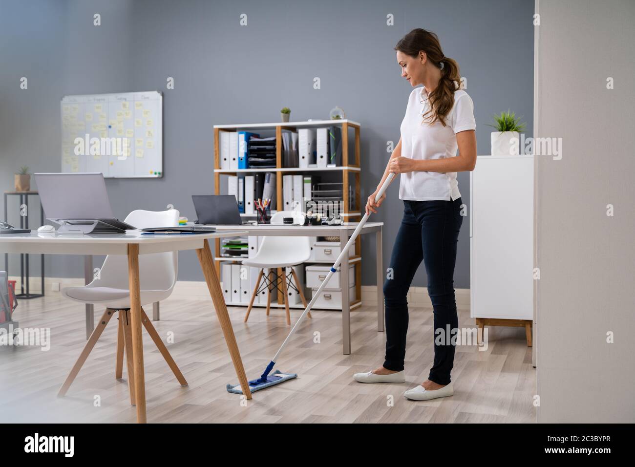 Full Length Of Female Janitor Mopping Floor In Office Stock Photo