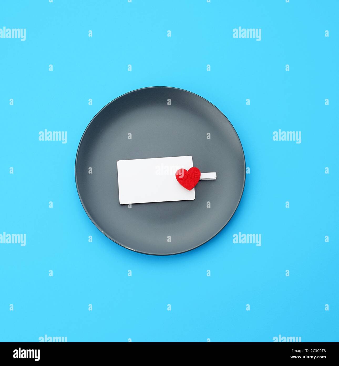 empty round gray plate and decorative red heart, next to an empty white business card, blue background Stock Photo