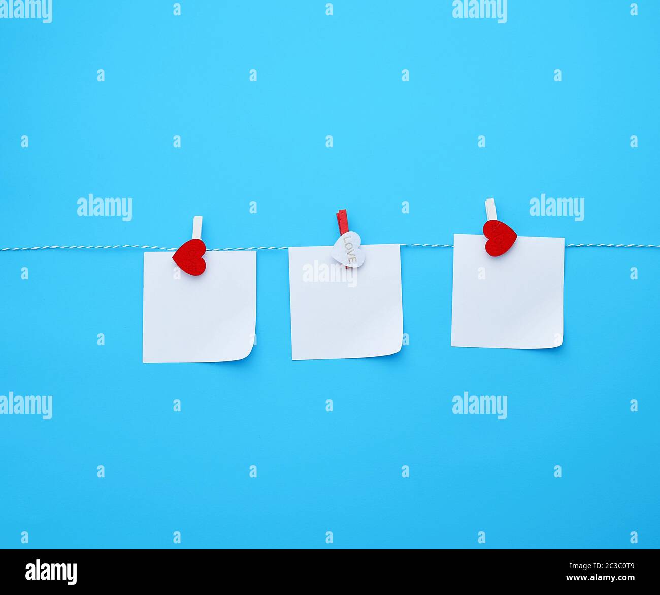 three empty square white paper sheets hanging on decorative clothespins, blue background Stock Photo