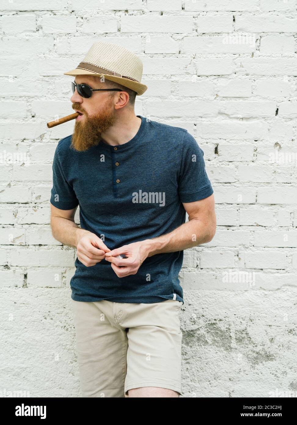 Young adult male wearing fedora and sunglasses smoking a cigar on the street. Stock Photo