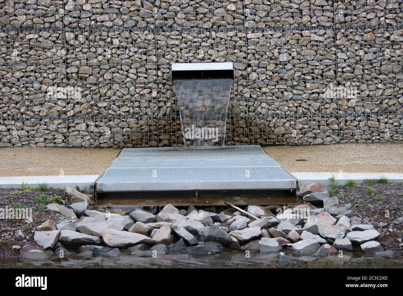 A stone wall built with gabions, from which water flows from Stock Photo