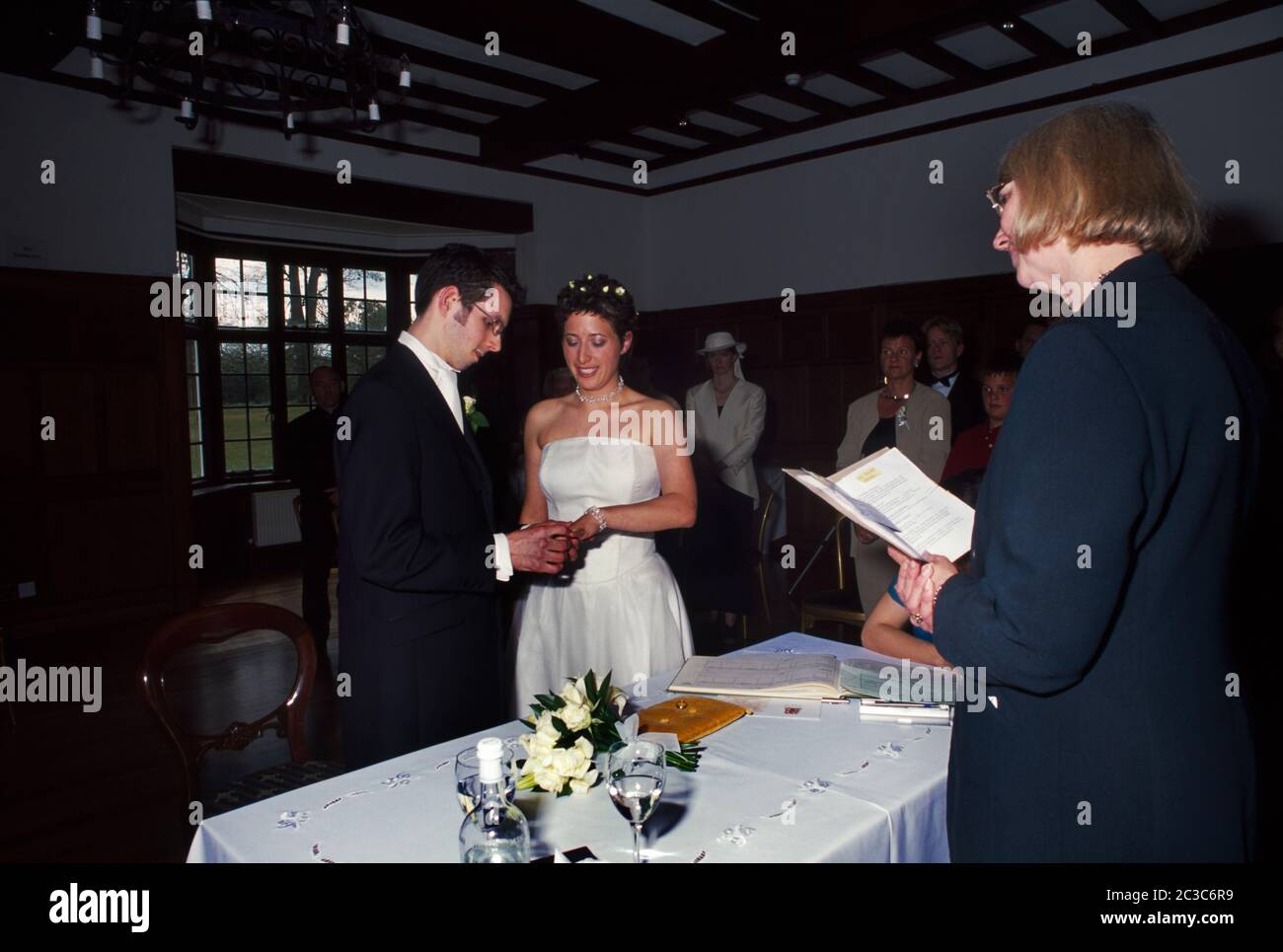 Bride and Groom In Their Twenties Exchanging Vows and Groom Placing Ring on Brides Finger Stock Photo