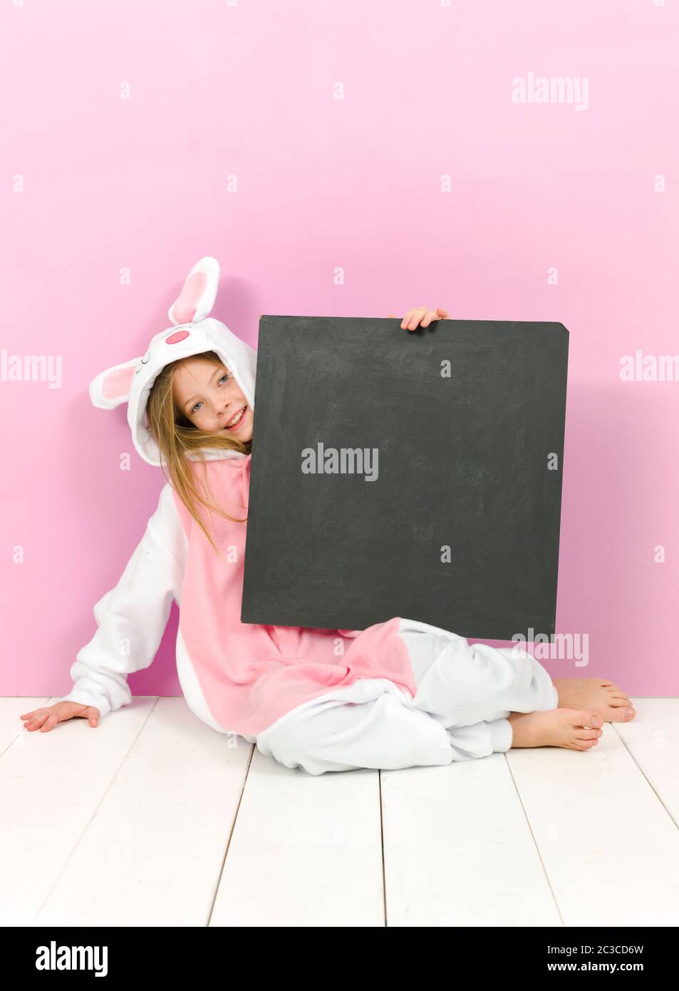 pretty blonde girl with cozy rabbit costume and blackboard is posing in the studio and is happy Stock Photo