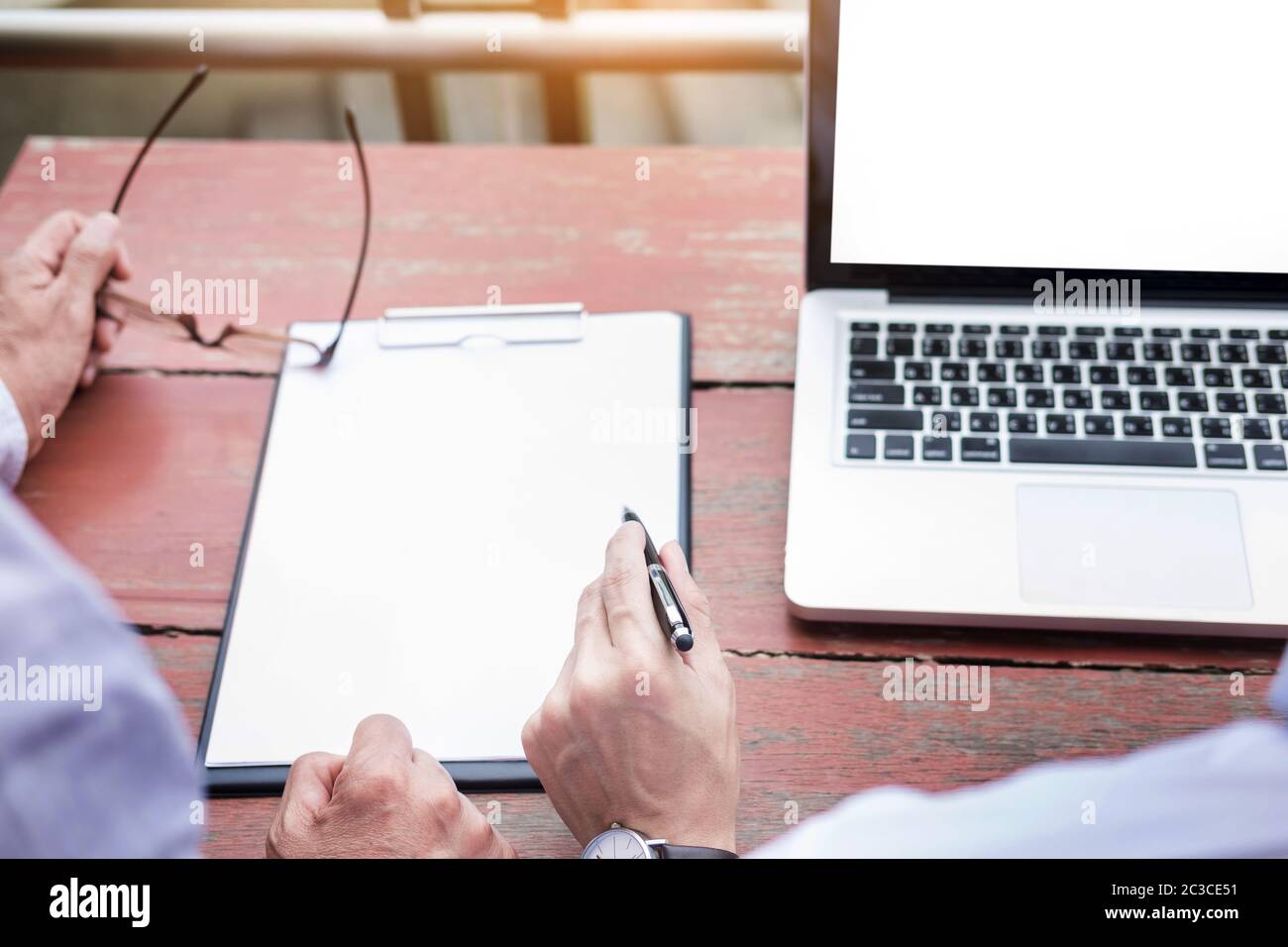 Two businessmen discussing planing tasks with laptop computer sitting at outdoor table. Stock Photo
