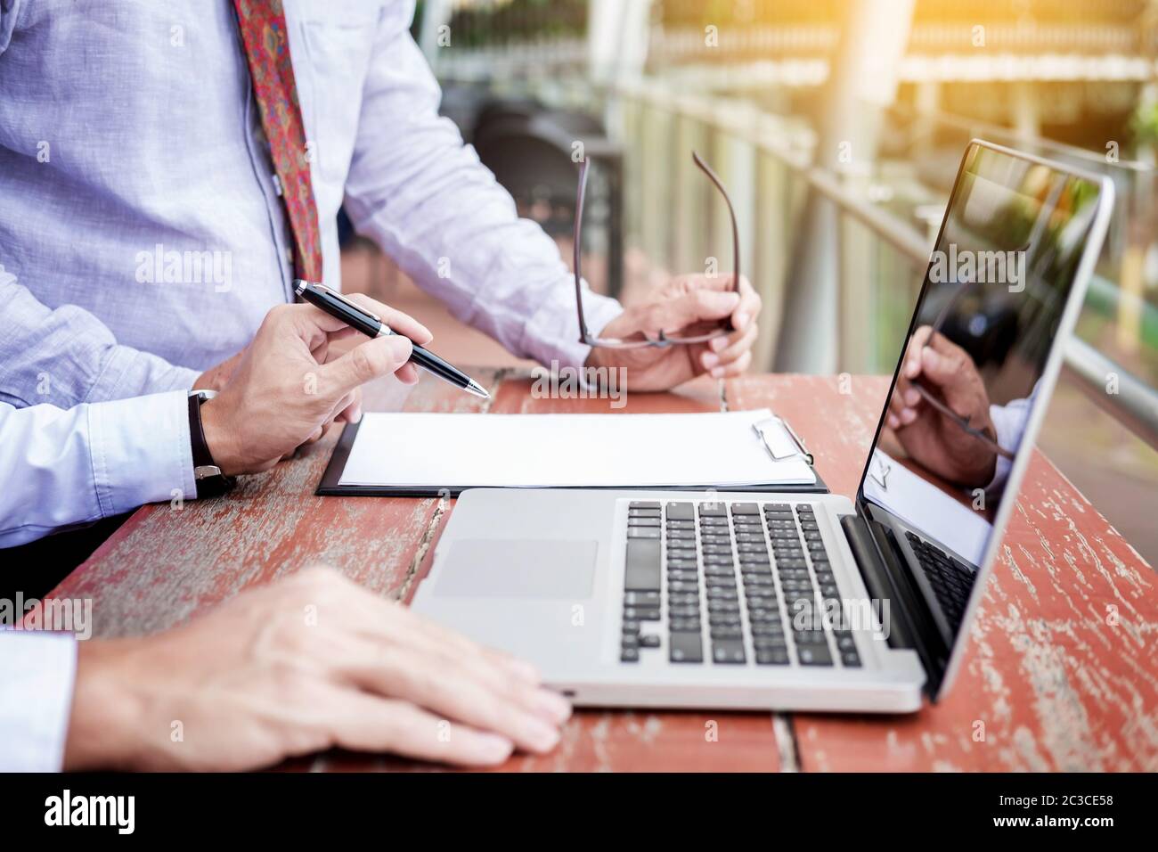 Two businessmen discussing planing tasks with laptop computer sitting at outdoor table. Stock Photo