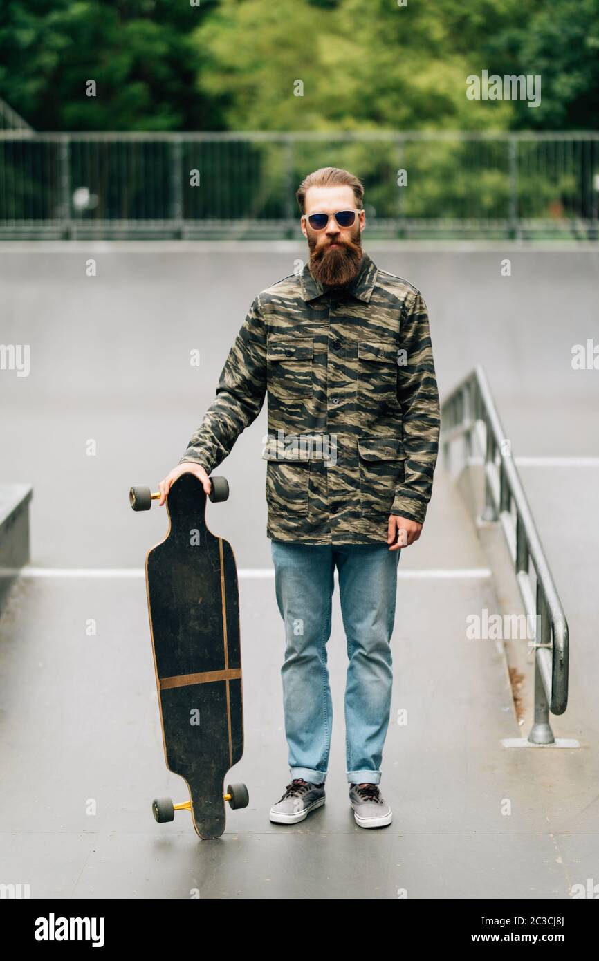 Bearded man holding longboard or skateboard in the park . Stock Photo