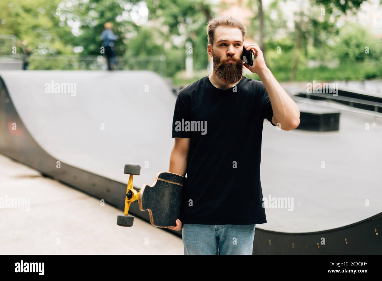 Young man with a skateboard is talking by a mobile phone while sitting in a skate  park on a sunny day Stock Photo - Alamy