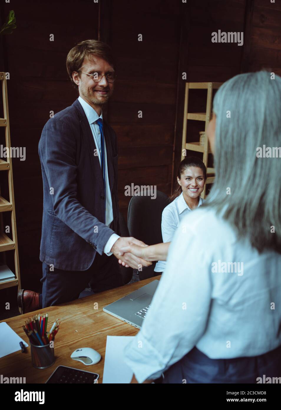 Business man and woman shaking hands while smiling and standing at office table. Handshake concept. Toned image Stock Photo