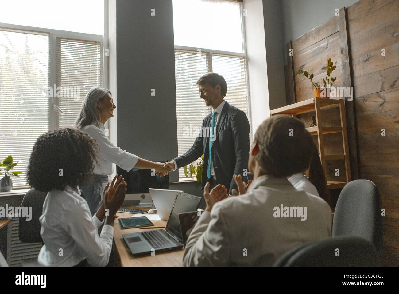 Business people shaking hands. Project manager shakes hands with employee to the applause of team sitting at negotiating table in office. Toned image Stock Photo