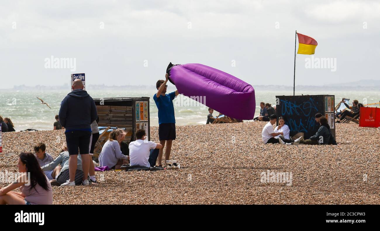 Brighton UK 19th June 2020 - It's not easy putting up a blow up seat on Brighton beach on a sunny but breezy afternoon on the seafront . The weather is forecast to get much warmer next week with temperatures expected to reach 30 degrees in parts of the South East  : Credit Simon Dack / Alamy Live News Stock Photo