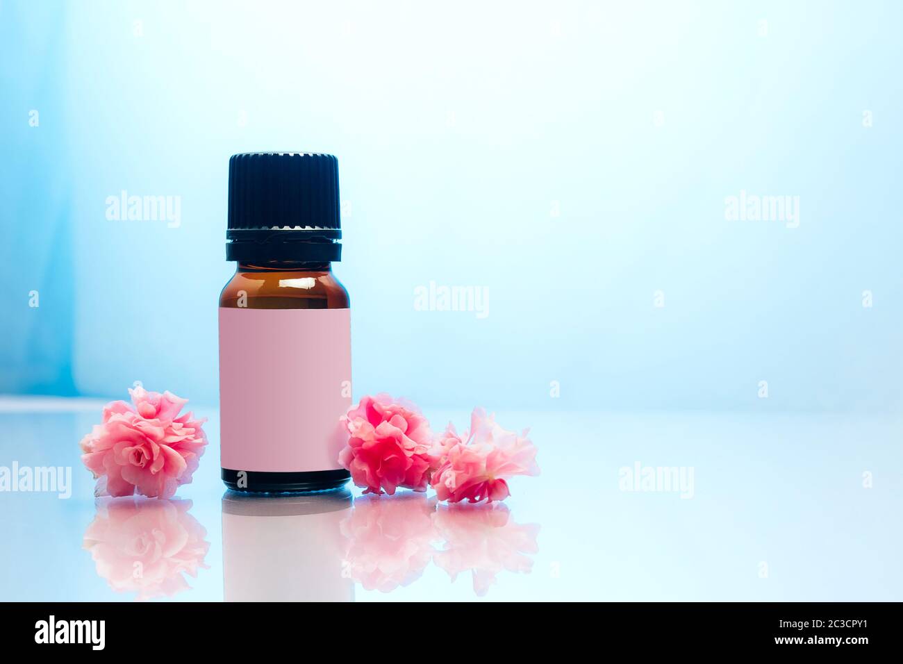 Bottle of essential oil with pink flowers on blue background. Stock Photo