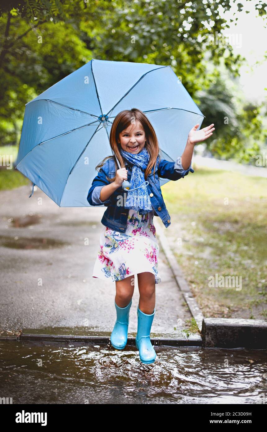 Cheerful small girl having fun in puddle on street Stock Photo