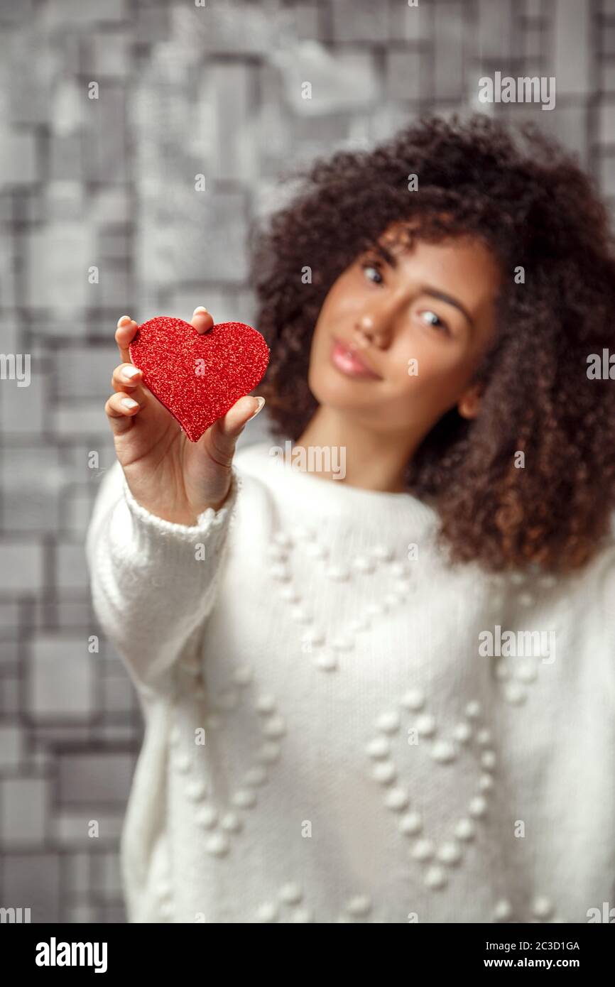 a paper red heart in the hands of a young African American curly-haired girl. focus on the heart, shallow depth of focus Stock Photo