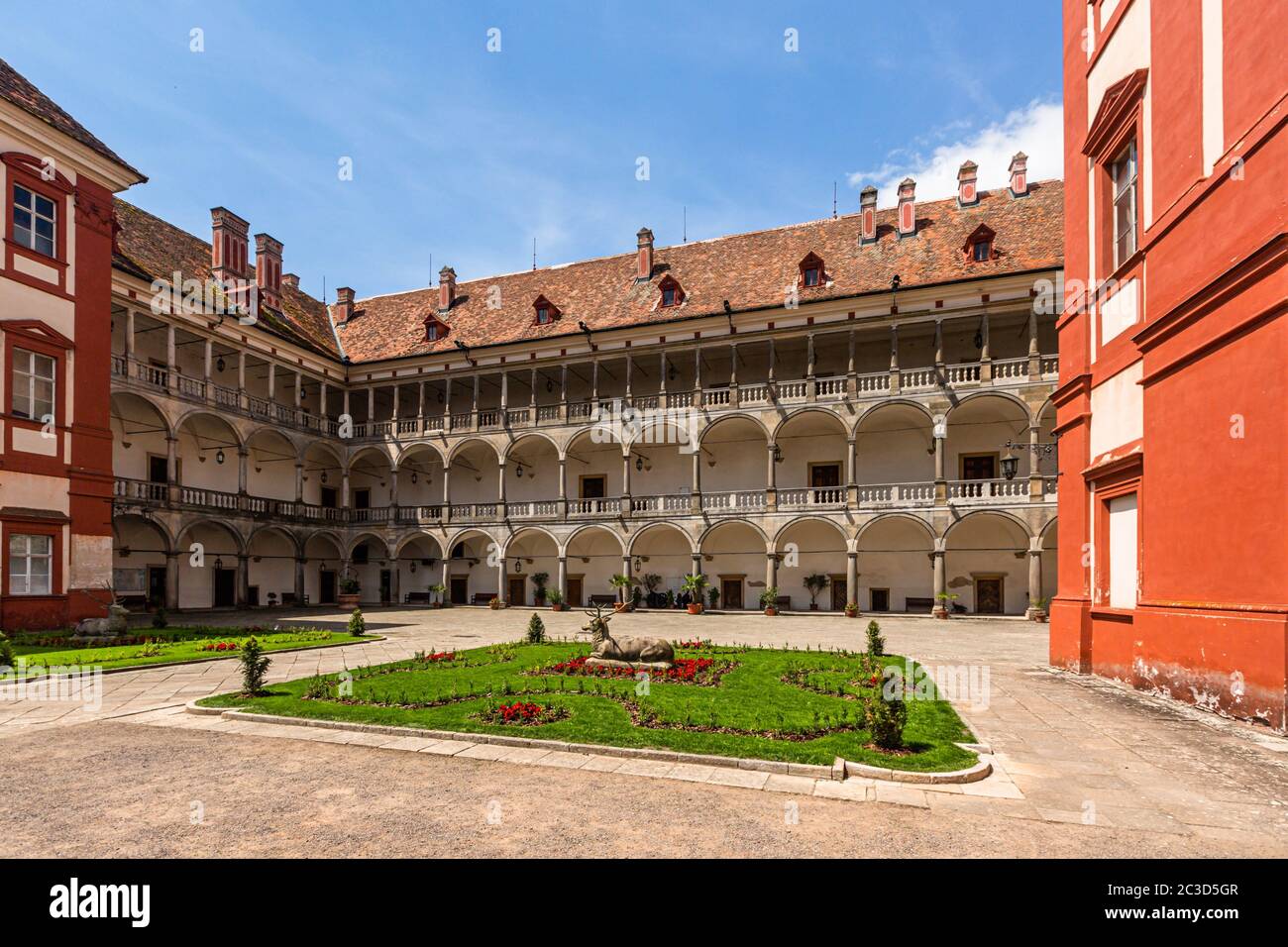 Opocno / Czech Republic - June 16 2020: View of the castle courtyard with arcades and red facade. Green lawn with statue and flowers in foreground. Stock Photo