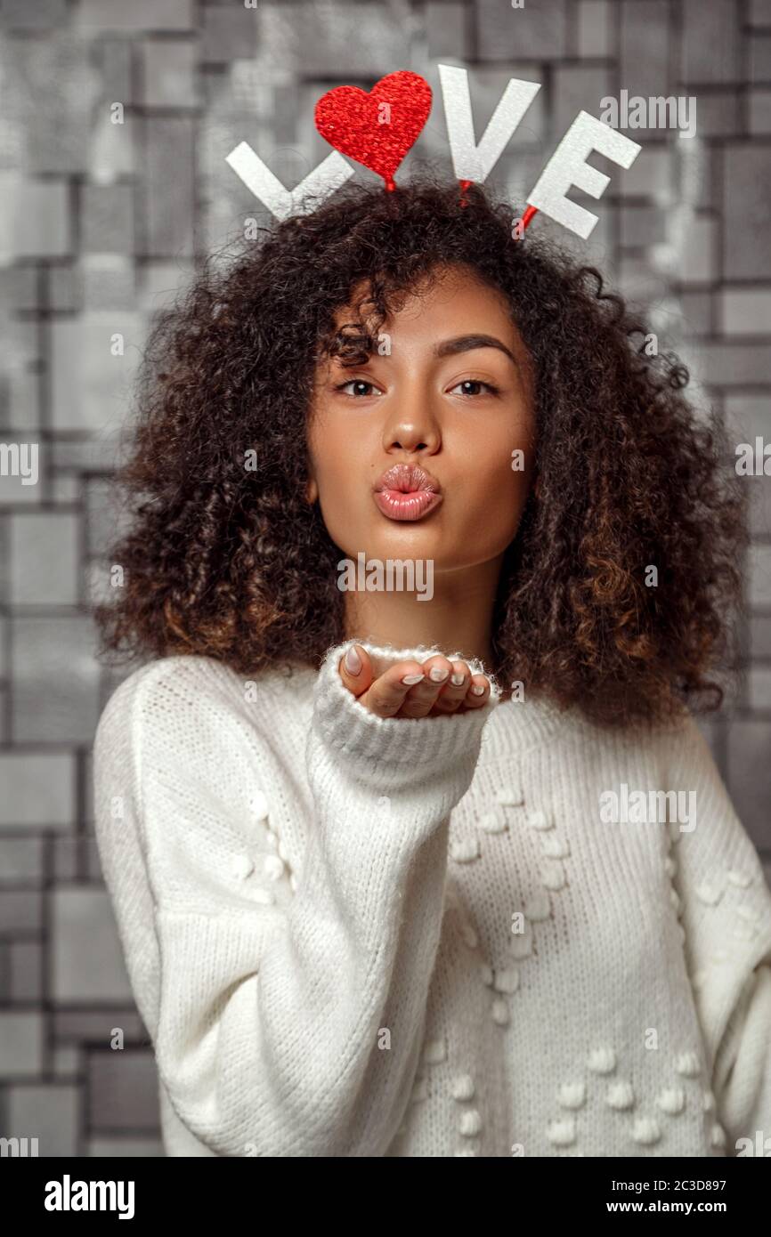a young beautiful curly haired girl with a rim with the inscription love on her head send a kiss through the air Stock Photo