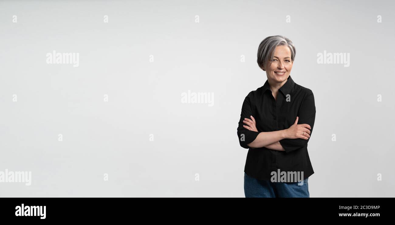Confident mature woman smiling arms crossed. Gray haired businesswoman in black shirt on white background. Horizontal template for ad banner with copy Stock Photo