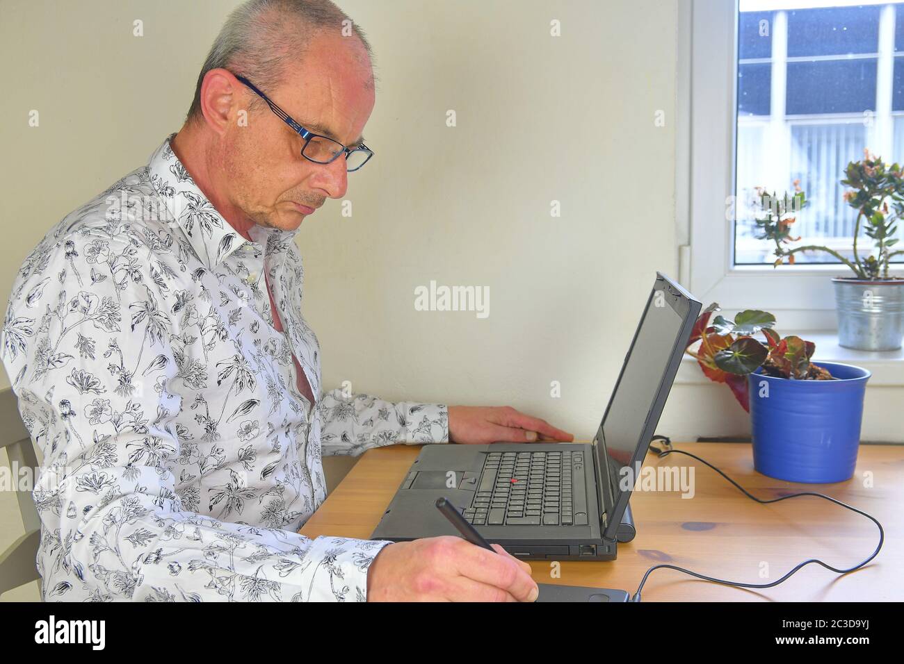 Mature man using a graphic pad and notebook in the home office. Graphic designer in home office sitting at desk using modern technology Stock Photo