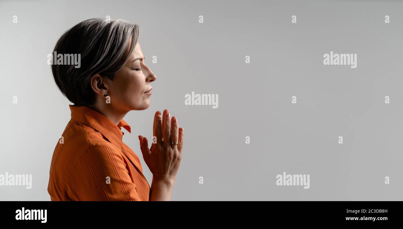Mature woman folded hands for prayer. Spiritual Caucasian woman closed eyes. meditation concept. Profile view. Horizontal template for ad banner with Stock Photo