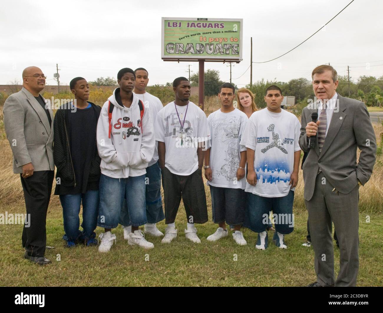 Austin Texas USA, 2008: Hispanic and African-American high school students and teachers stand under school dropout prevention billboard they designed, as TV news reporter speaks into camera in front of them.  ©Marjorie Kamys Cotera/Daemmrich Photography Stock Photo