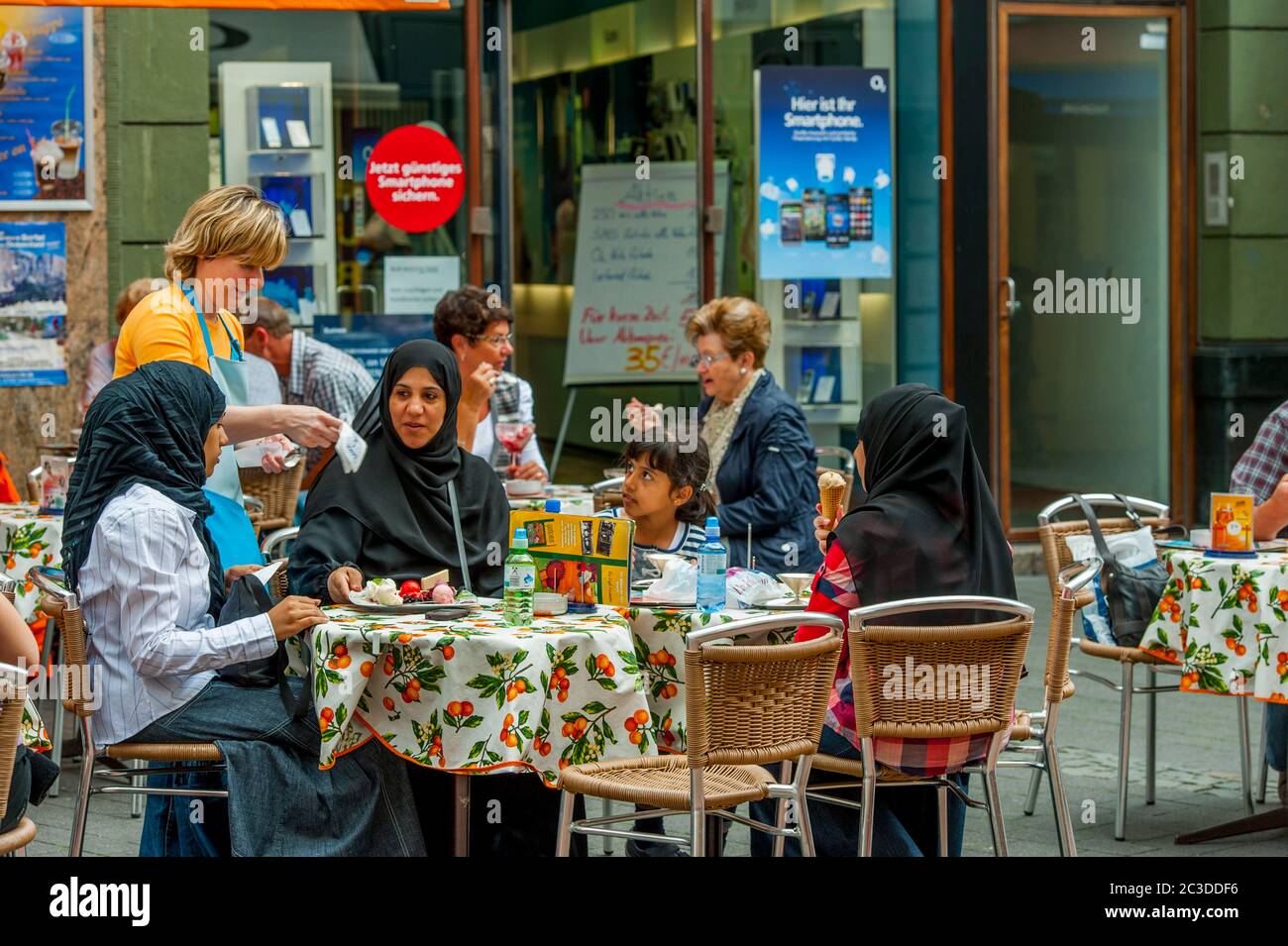 A Muslim family is having water and ice-cream in a sidewalk cafe in Bonn, Germany. Stock Photo