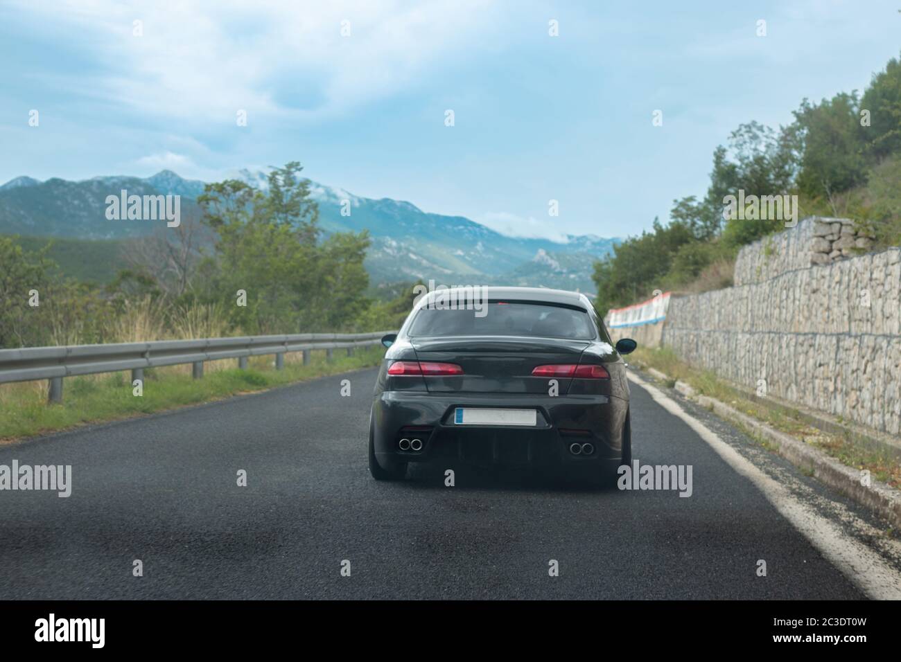 Rear view of a black modified old italian car driving through south ...