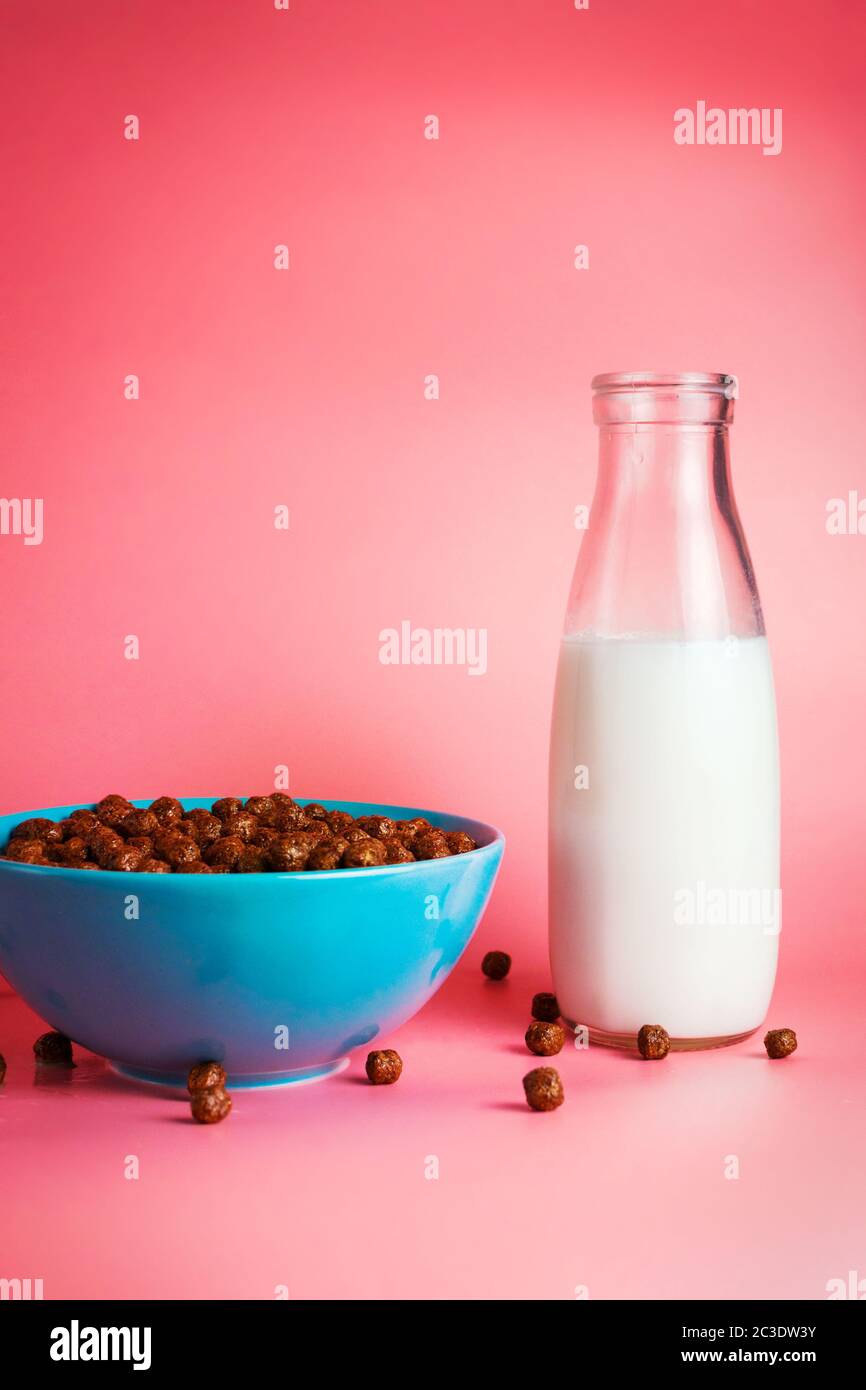 Plank milk in a glass bottle and chocolate breakfast cereals in a blue bowl on pink background. Selective focus Stock Photo