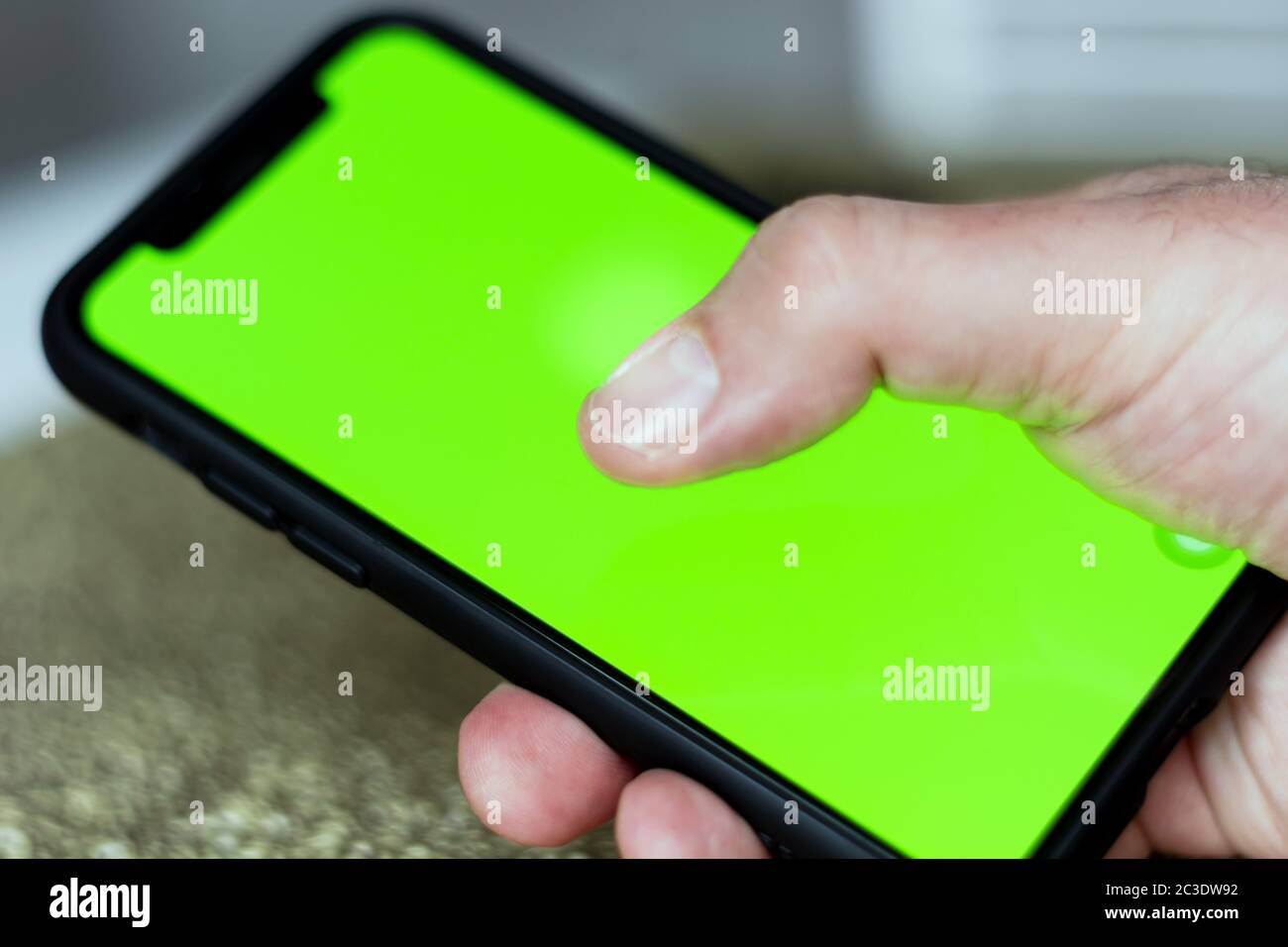 the thumb of a male hand while touching the green screen of a mobile phone. Stock Photo