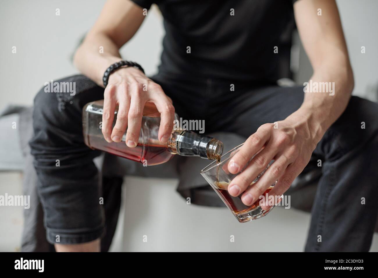 Closeup of unrecognizable man in black jeans pouring whisky into glass