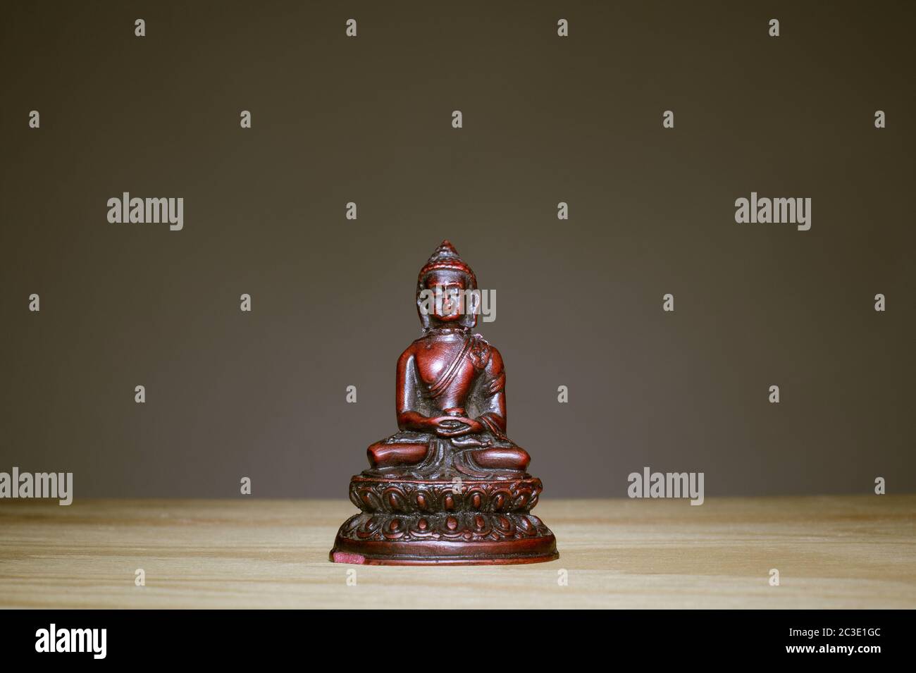 Small figurine of Buddha on wooden desk. Unicolor grey background. Pose of meditation and relaxation. Copy space Stock Photo