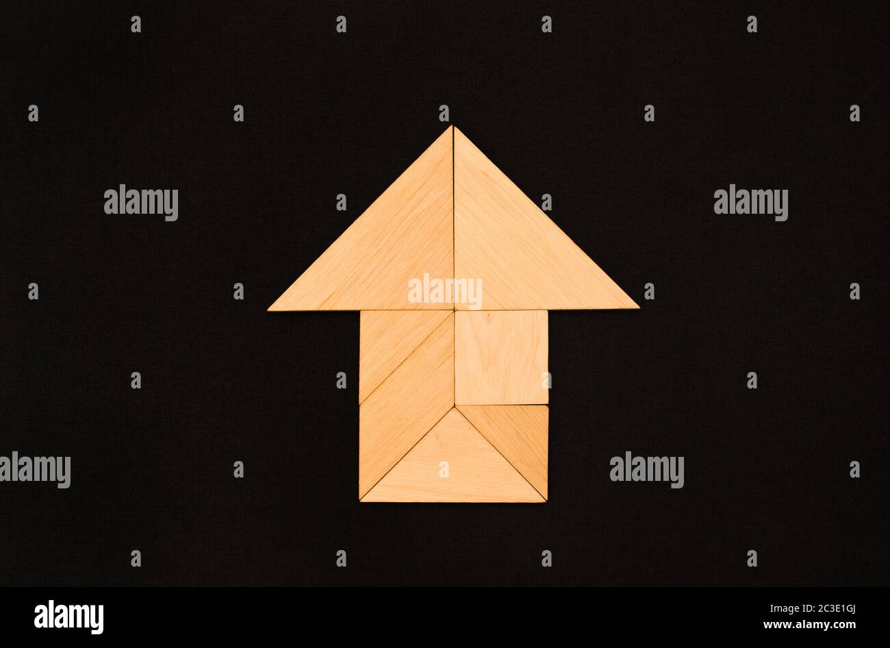 Flat lay - pictogram, symbol, icon of house and arrow made of wooden tangram pieces. Unicolor background made of dark fabric texture. Stock Photo